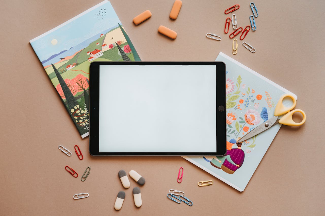Flat lay of colorful stationery with tablet, notebooks, and scissors, ideal for education themes.